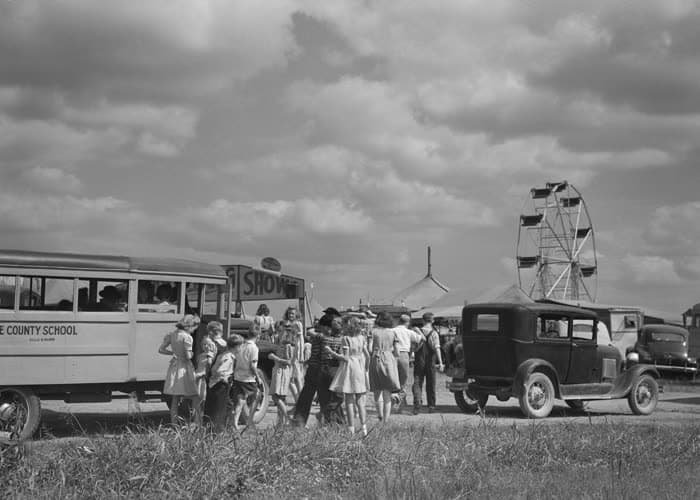 Families arriving at the fair by school bus and car, the Ferris wheel on the horizon